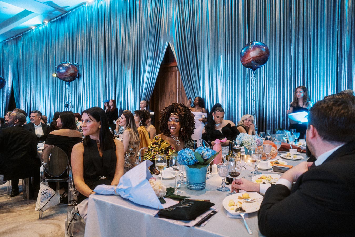 Guests enjoying a festive dinner event with elegant decor featuring silver drapes and floral centerpieces.