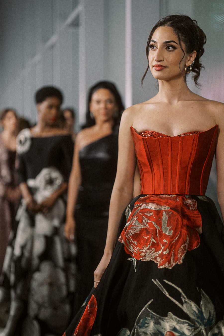 Fashionable woman in a red floral gown leading a line of stylishly dressed individuals at a formal event.