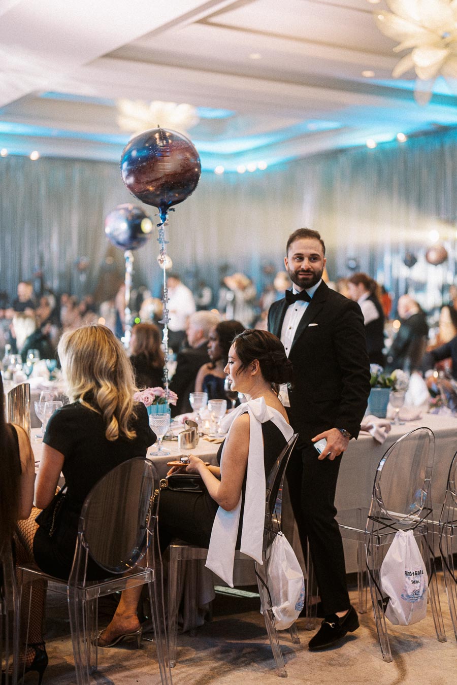 Elegant indoor event with people in formal attire, seated at decorated tables with unique celestial-themed balloons, creating a sophisticated and festive atmosphere.
