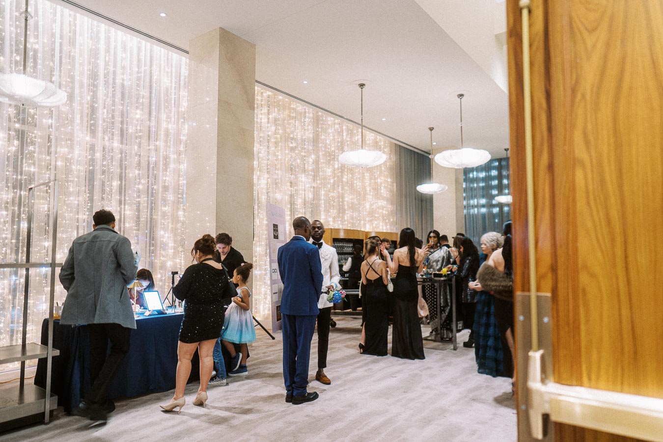 Elegant evening event with guests socializing in a luxurious setting, featuring warmly lit drapery and modern decor.