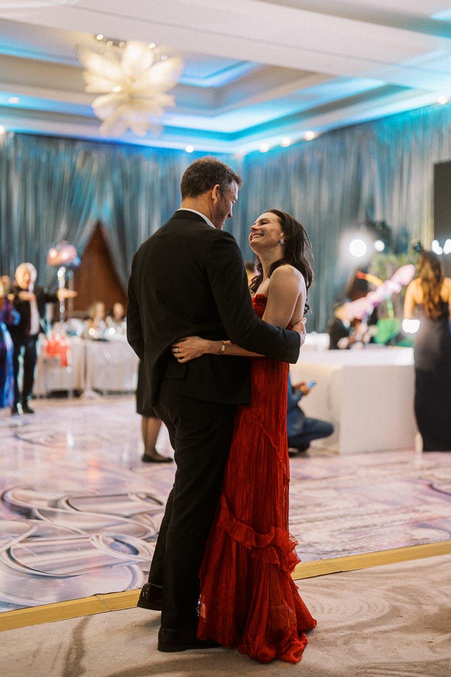 Elegant couple dancing and smiling in a beautifully decorated ballroom setting.