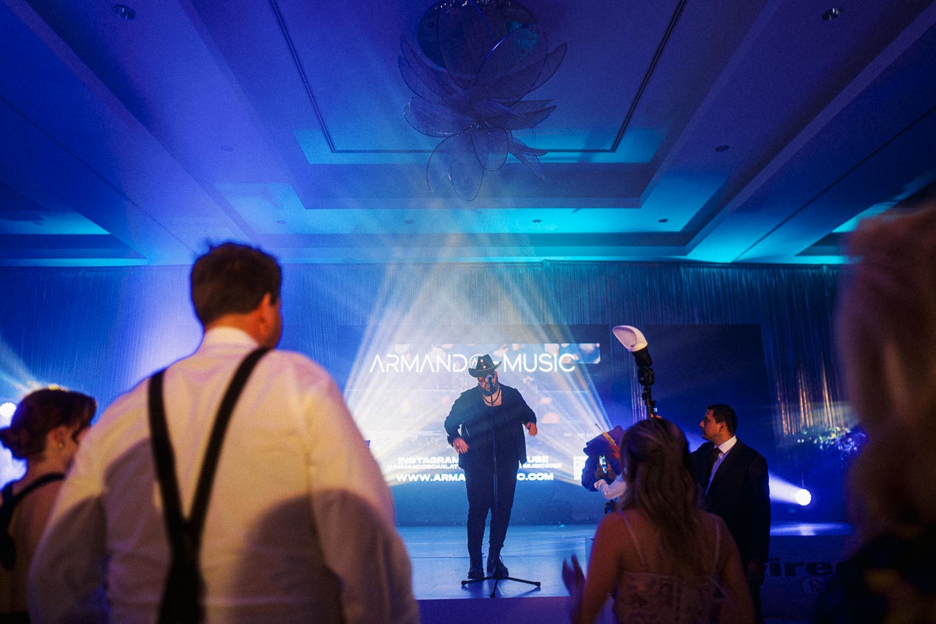 Live music performance with a singer on stage under blue lighting, Armanda Music displayed in the background, audience enjoying the show.