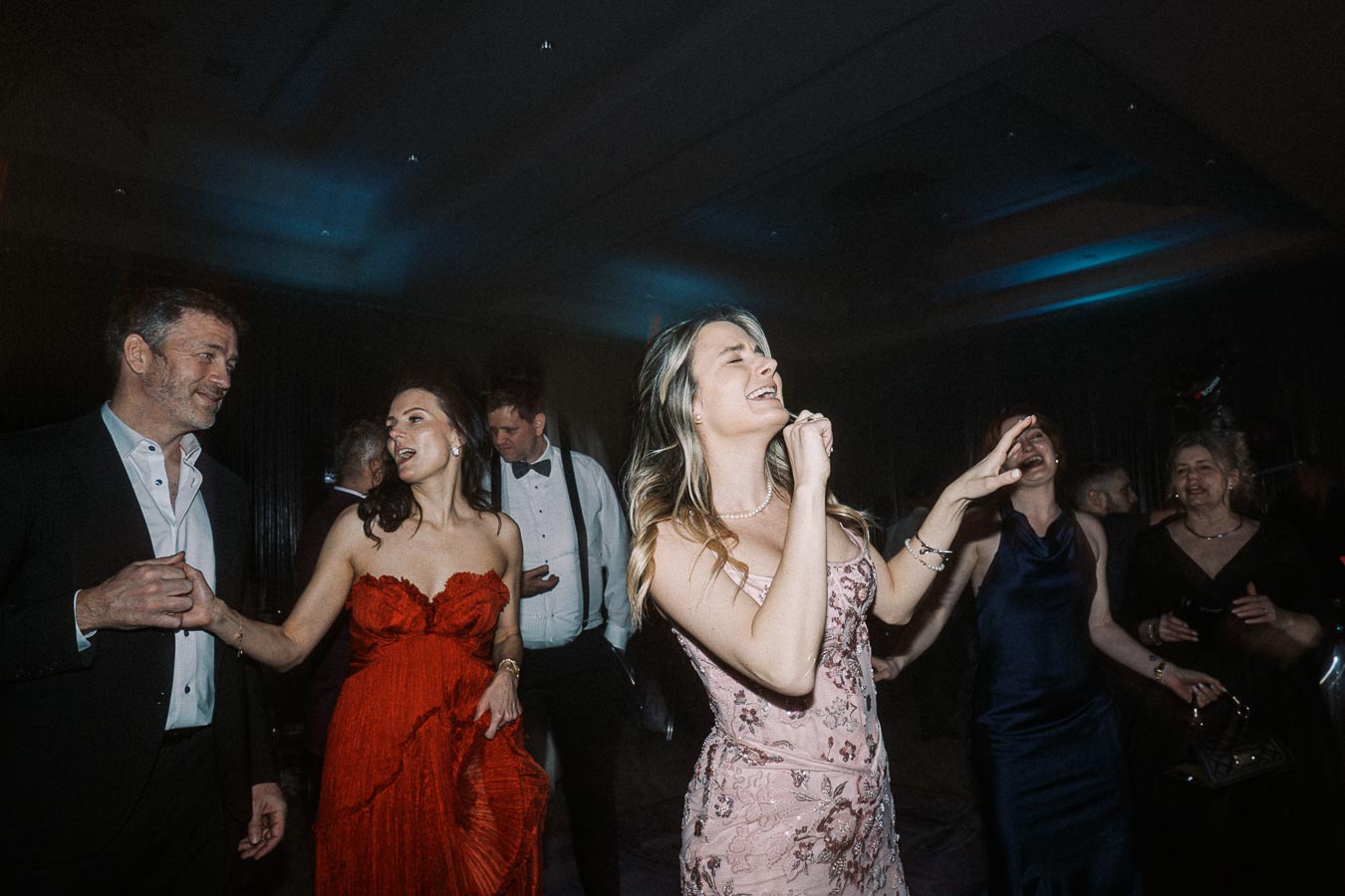Group of elegantly dressed people enjoying a lively evening on the dance floor at a formal event.