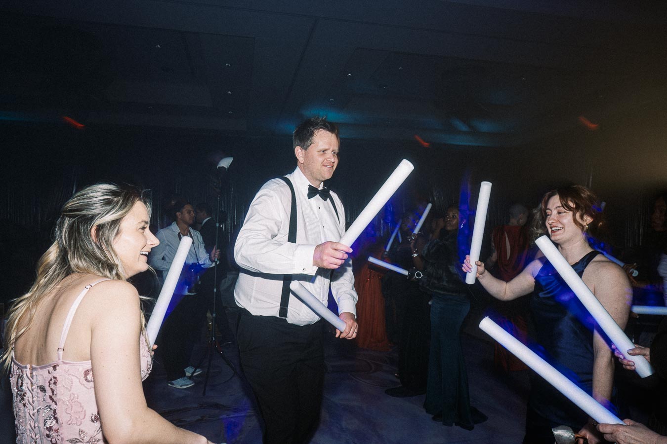 People enjoying a lively dance party, holding glowing foam sticks in a dimly lit venue.