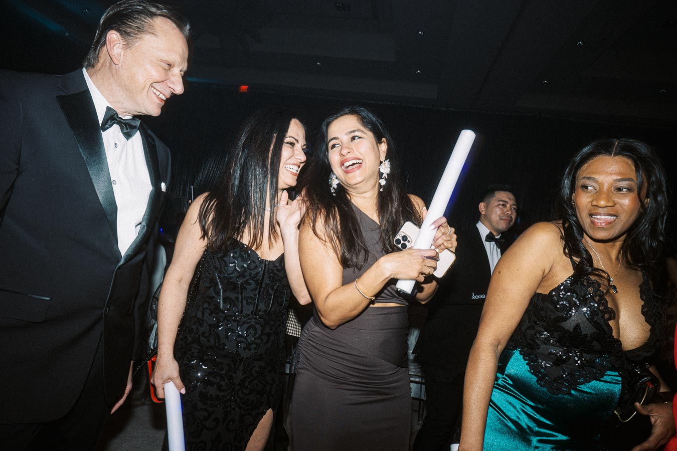 Elegant group of people enjoying a formal event, laughing and socializing in fashionable evening attire.