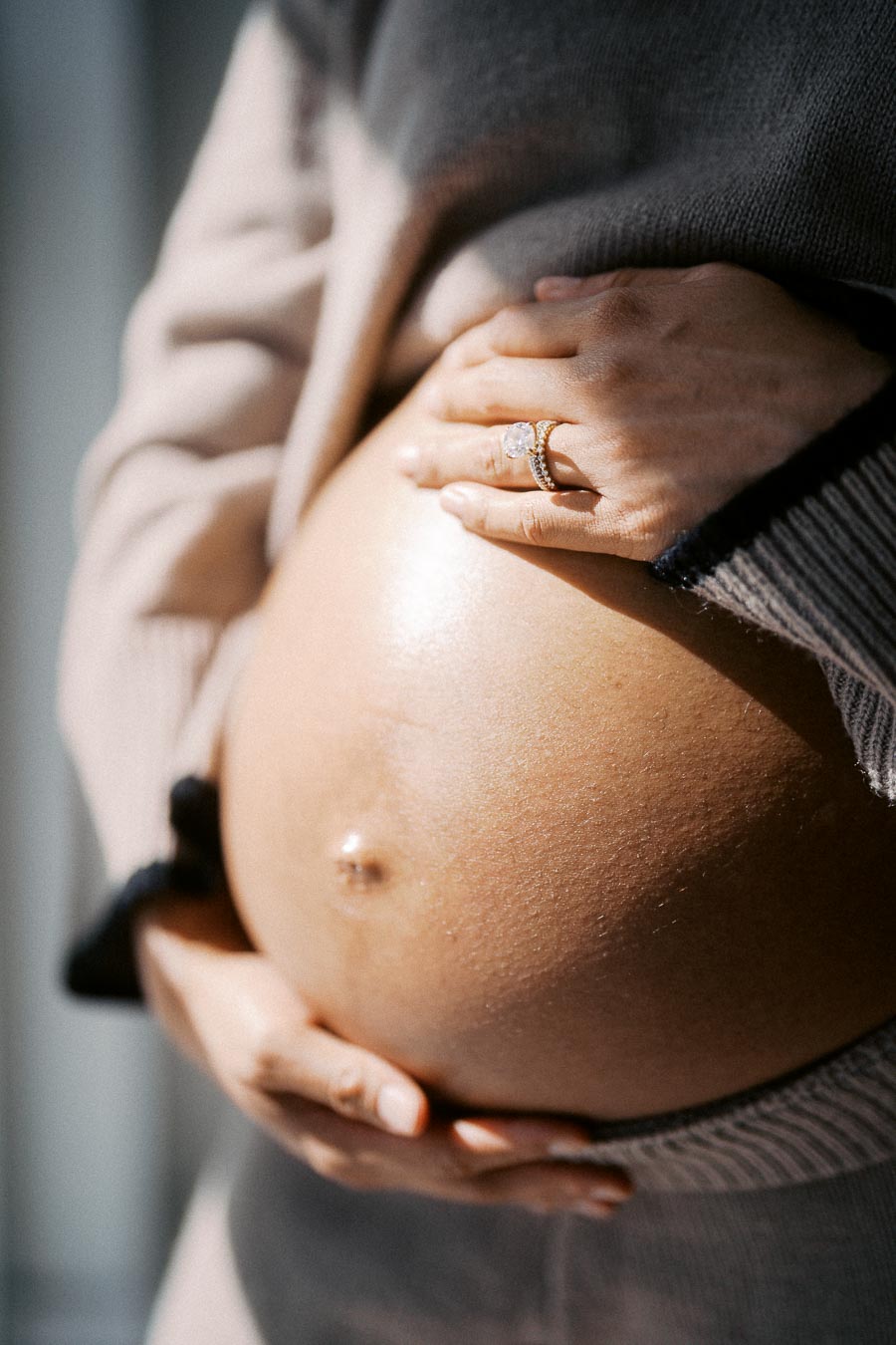 Close-up of a pregnant woman gently holding her belly, highlighting a gold ring on her finger.