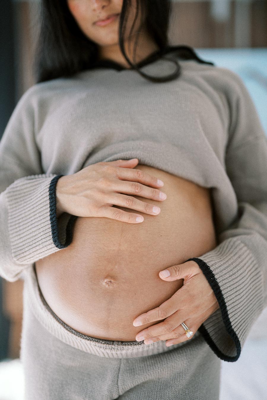 Pregnant woman gently holding her belly, wearing a cozy gray sweater, symbolizing motherhood and wellness.