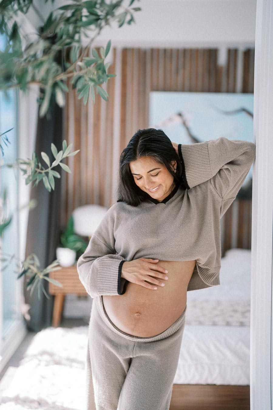 Pregnant woman smiling and touching her belly in a cozy, light-filled room.