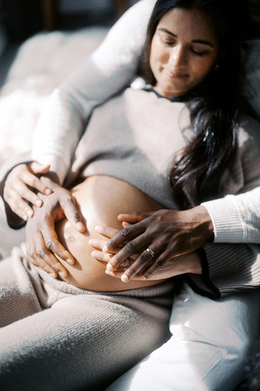 Pregnant woman smiling with partner's hands on her belly, highlighting love and connection during pregnancy.