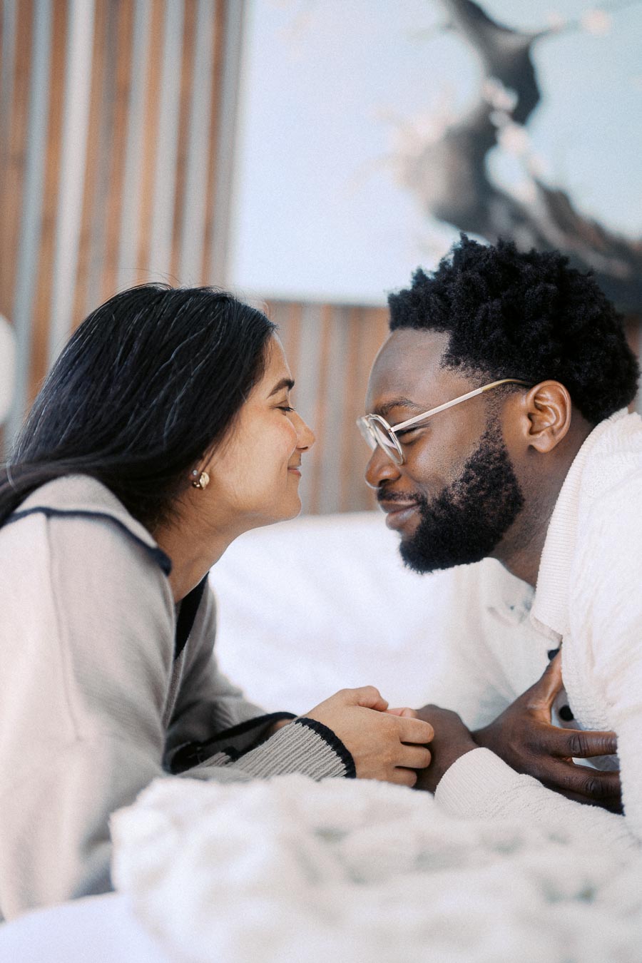 A couple smiling and holding hands while facing each other indoors, conveying warmth and intimacy.