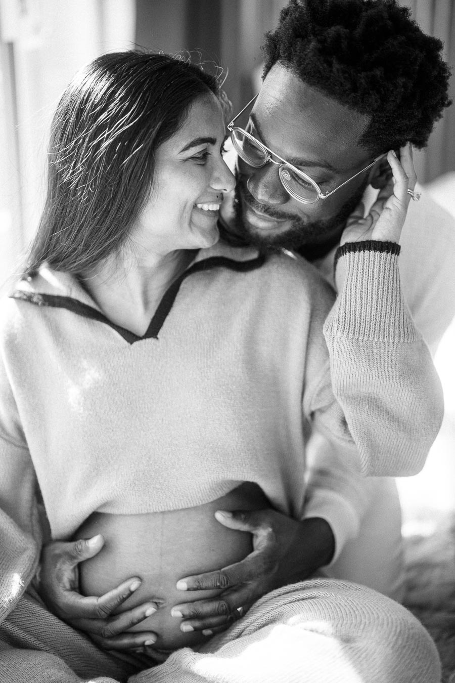 Happy couple sharing an intimate moment, with the man gently holding the woman's pregnant belly, expressing love and anticipation for their future together.