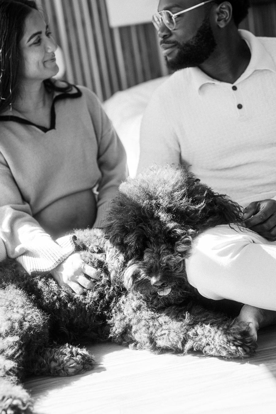 A black and white photo of a couple sitting closely with a large fluffy dog, creating a warm and cozy atmosphere.