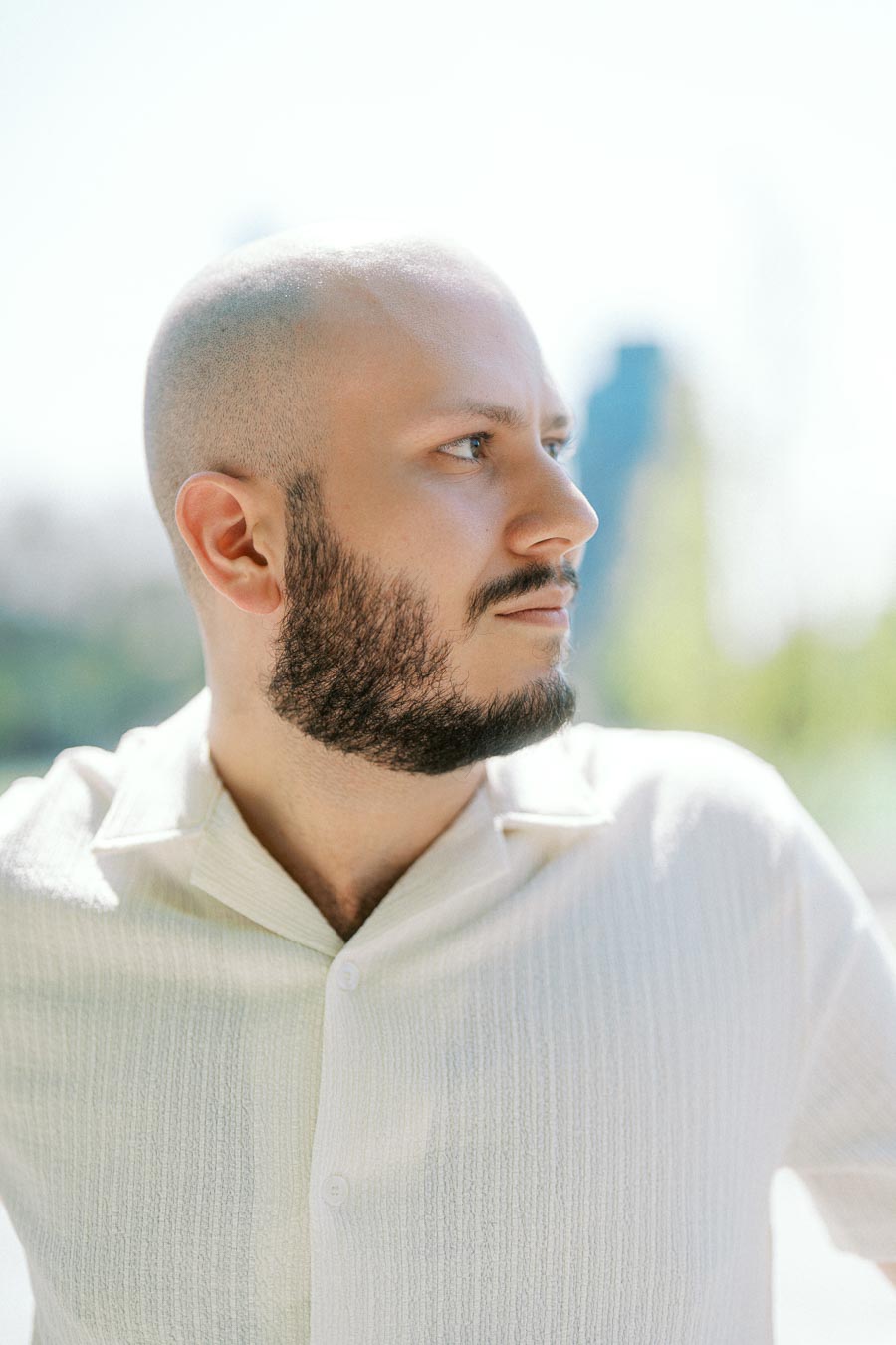 Close-up of a man with a beard and light shirt looking to the side in bright spring light at the University of Toronto campus.