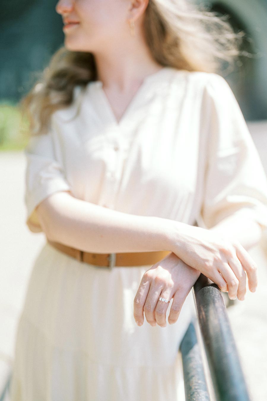 Bride-to-be leans on a rail, showing her engagement ring in soft sunlight at the University of Toronto campus.