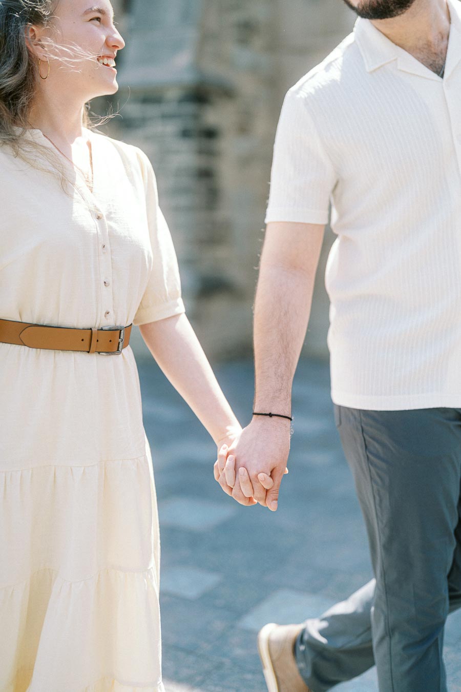 Couple holding hands and smiling while walking outdoors in spring sunlight at the University of Toronto campus.