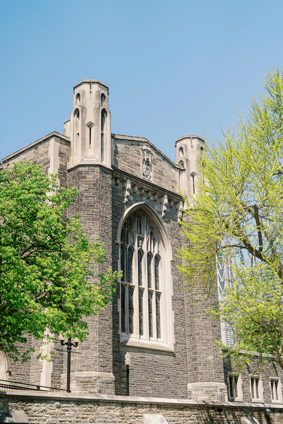 Historic Hart House building at University of Toronto, framed by blooming green trees and bright spring sunlight.