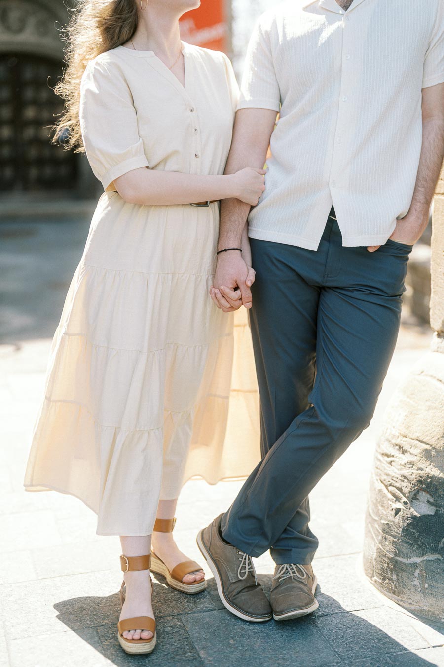 Couple holding hands and linking arms in soft sunlight at the University of Toronto, dressed in light spring outfits, showing a warm connection.