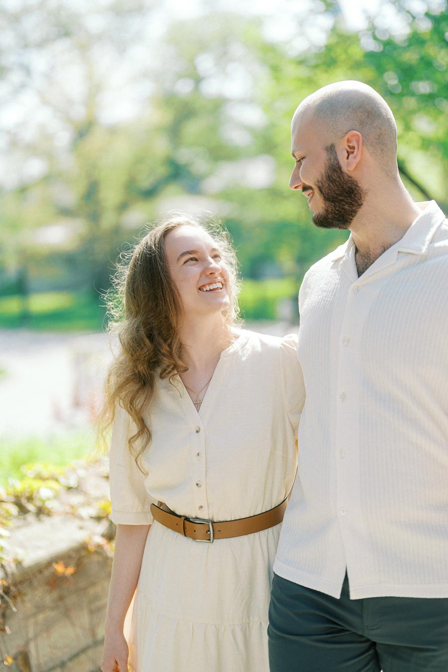 Couple smiling at each other, enjoying a candid moment in spring sunlight at the University of Toronto campus.