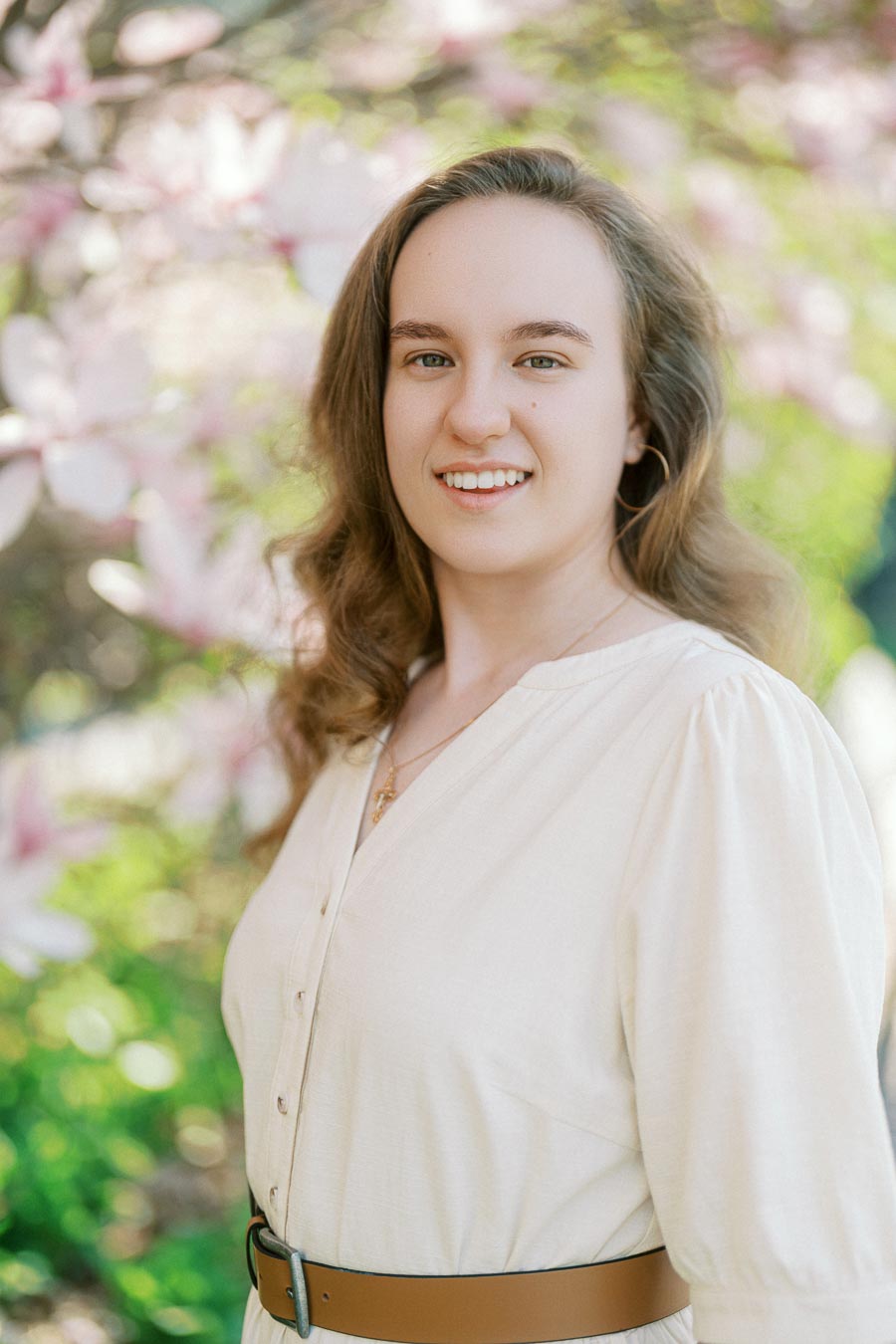 Woman smiling in soft natural light, standing among blooming pink and white spring flowers on the University of Toronto campus.