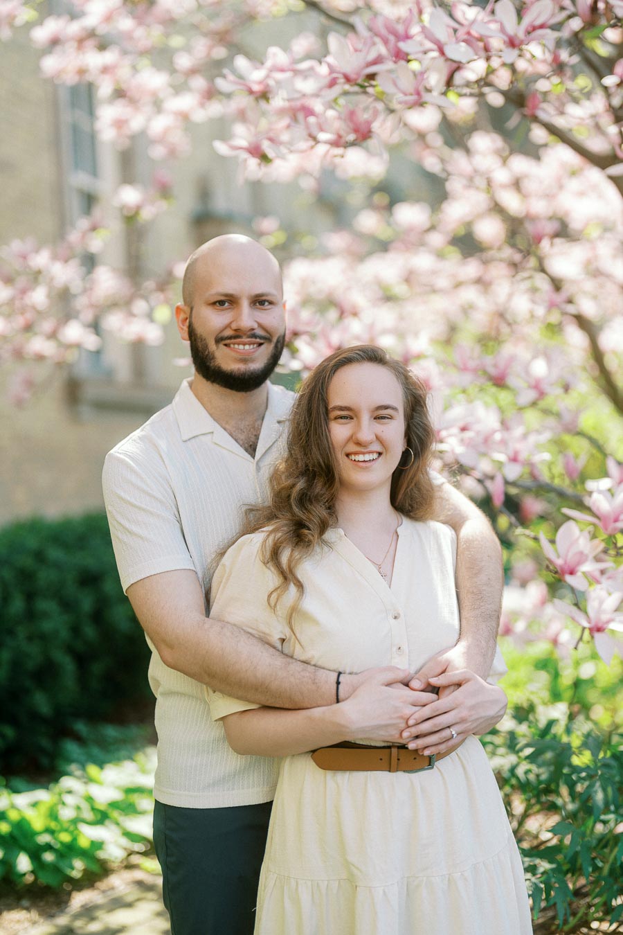 Couple smiling and embracing under blooming magnolia trees at University of Toronto during a spring engagement session.