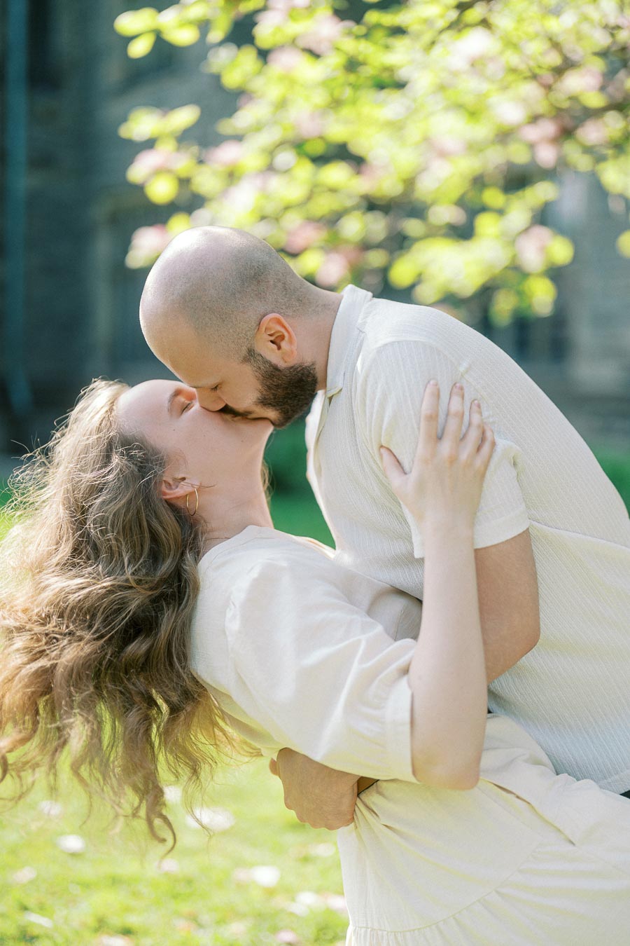 Couple sharing a romantic dip and kiss under blooming spring trees at the University of Toronto campus.