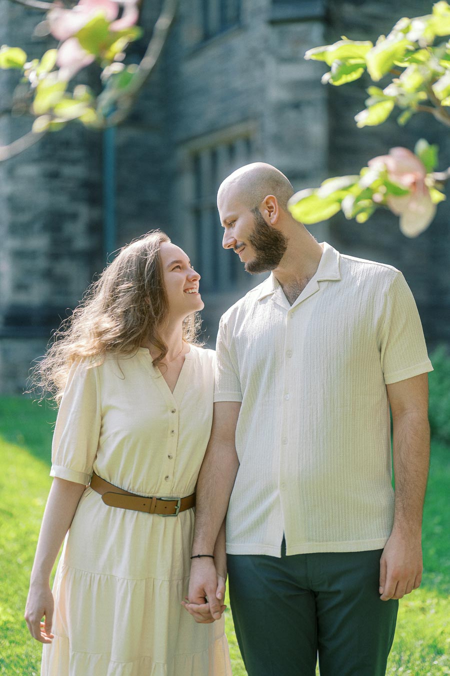 Couple holding hands and smiling at each other under blooming trees on a sunny spring day at the University of Toronto.
