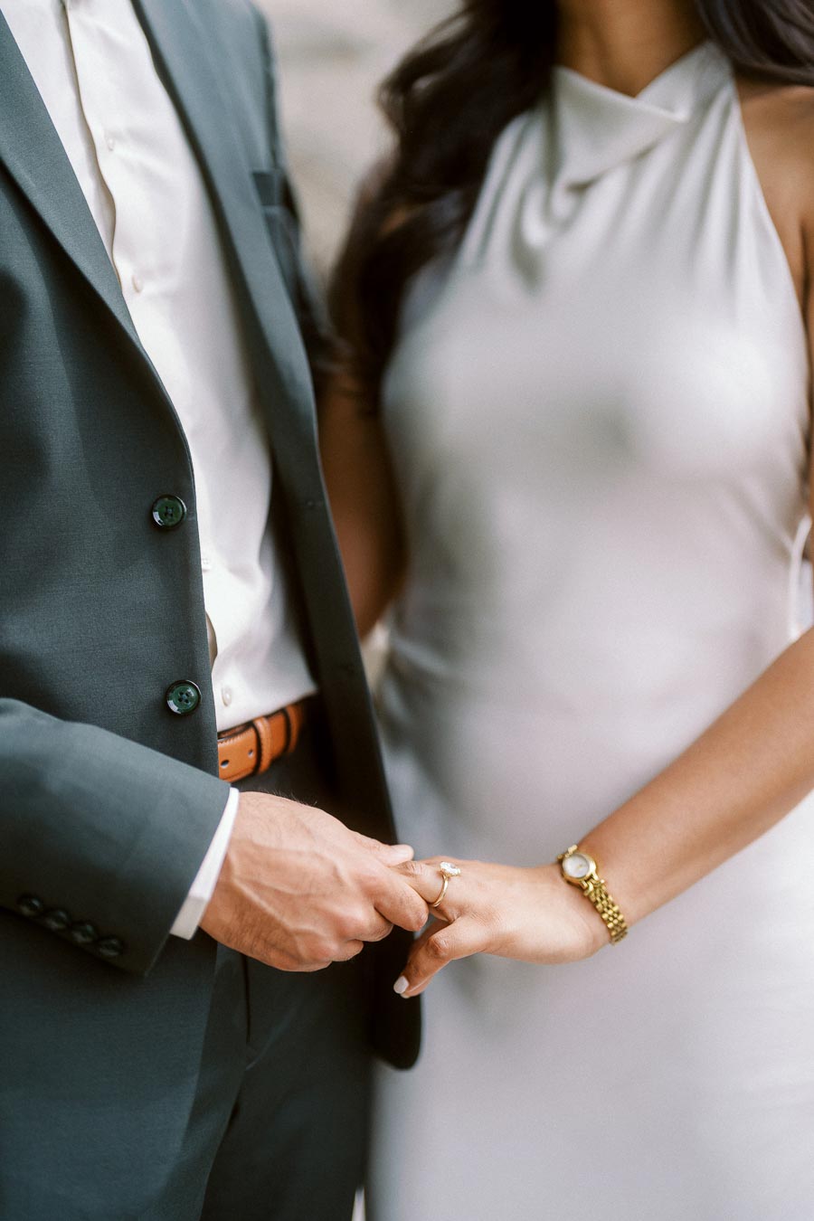 Close-up of a man placing an engagement ring on a woman's finger, both dressed formally, during an engagement session at University of Toronto.