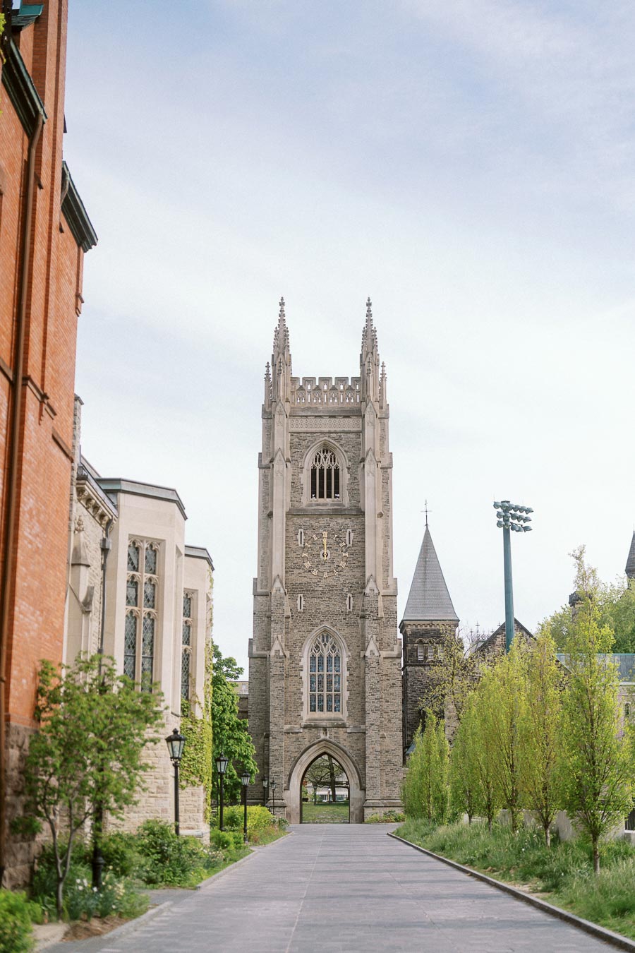A tall historic stone tower with Gothic architectural details stands at the University of Toronto St. George campus, framed by greenery and campus buildings.