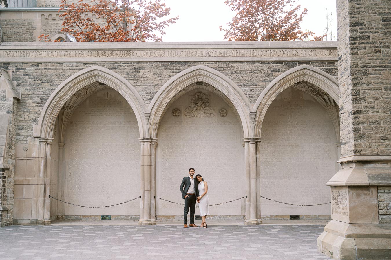 A couple stands together under large Gothic stone archways at the University of Toronto St. George campus.