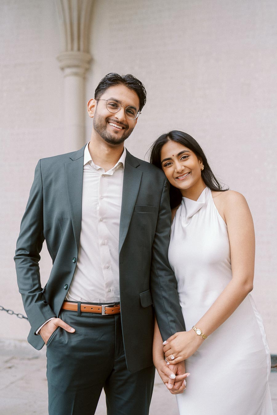 Tej and Priyana stand together holding hands, smiling, during their engagement session at the University of Toronto St. George campus.
