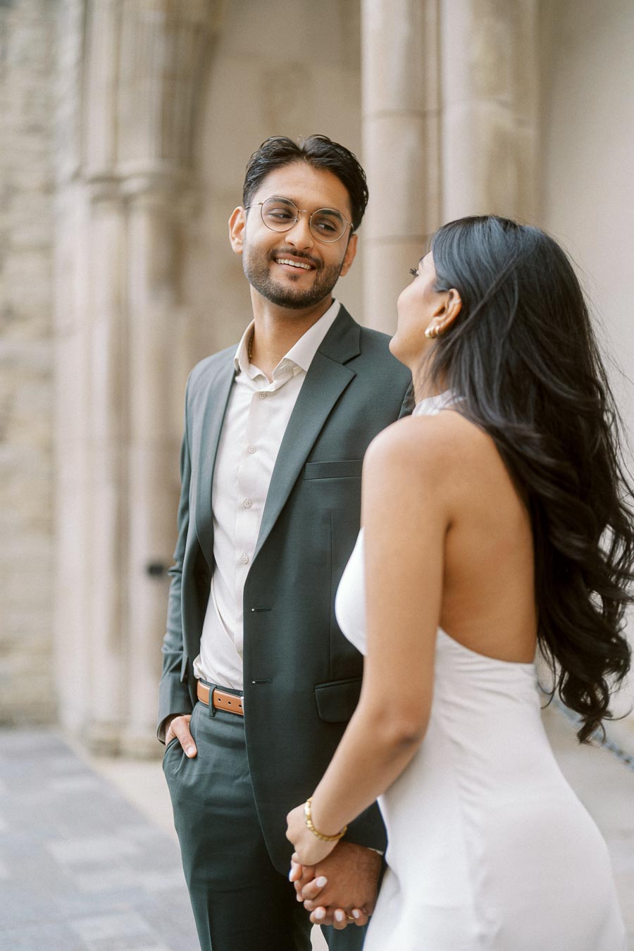 Tej and Priyana holding hands and looking at each other while standing beside a stone archway at the University of Toronto.