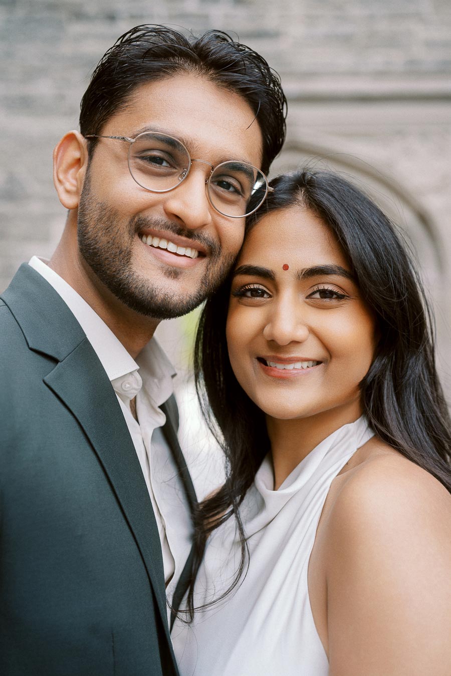 A close-up of Tej and Priyana smiling together during their engagement photoshoot at the University of Toronto, with stone architecture in the background.