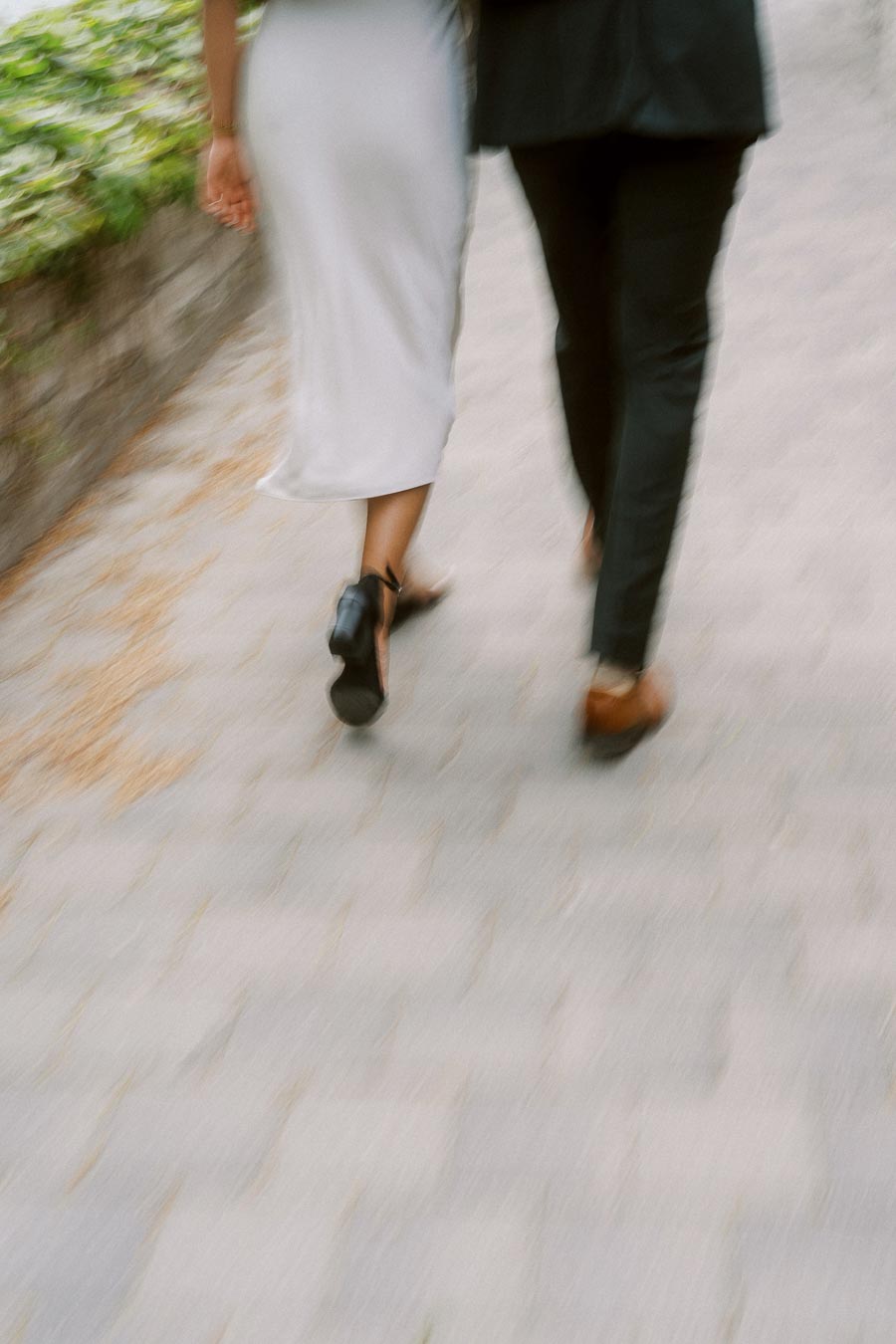 Motion-blurred view of a couple walking side by side on a paved campus path, with greenery on the left, at the University of Toronto.