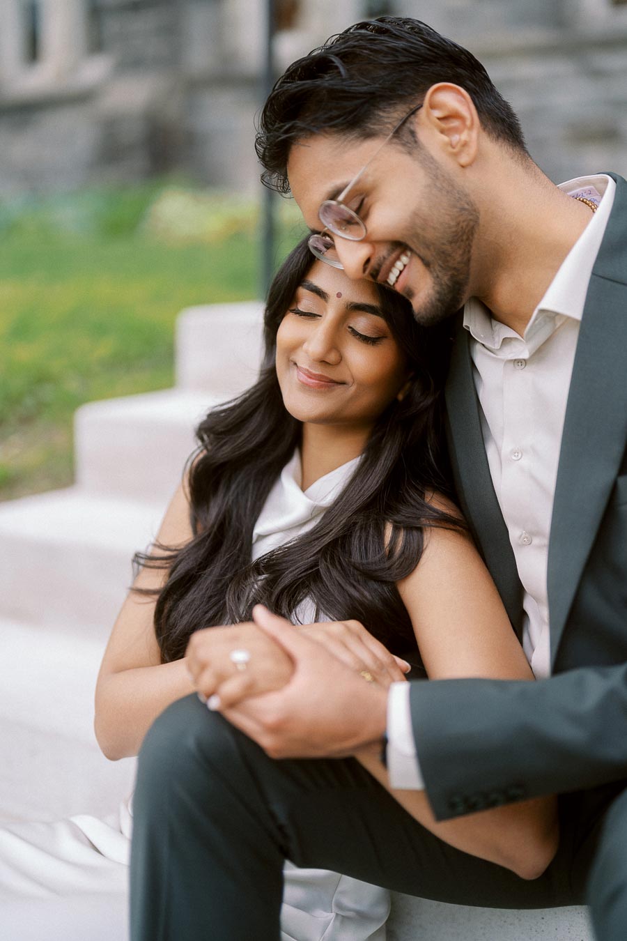 Tej and Priyana seated closely on stone steps at the University of Toronto, with Tej leaning his head affectionately against Priyana.