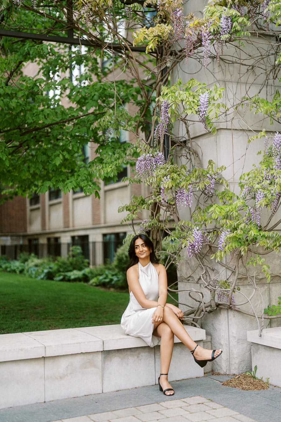 Priyana sits on a stone bench next to blooming wisteria vines and greenery at the University of Toronto campus.
