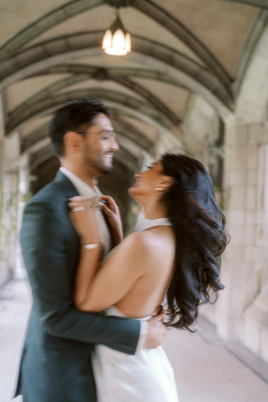 A couple stands close together, smiling and embracing under a stone archway at the University of Toronto St. George campus.
