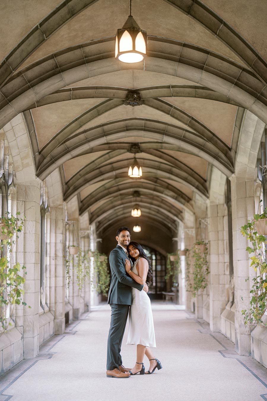 Tej and Priyana stand embracing under a vaulted stone archway with greenery at the University of Toronto St. George campus.