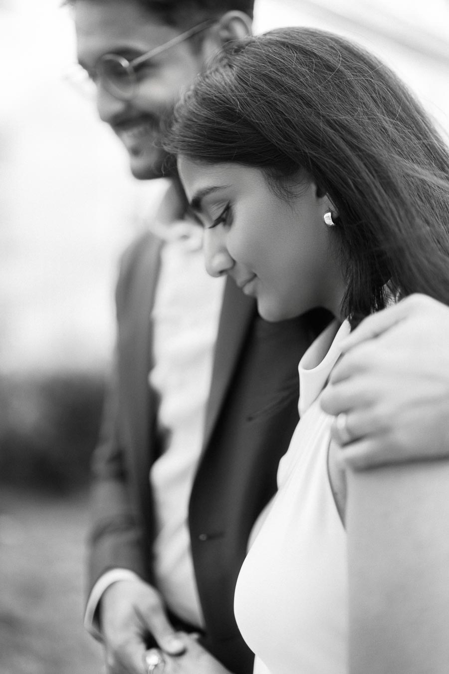 A close-up black and white portrait of an engaged couple, with the man gently holding the woman's shoulder at the University of Toronto.