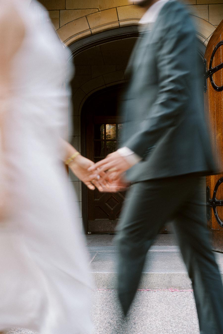 A blurred image of a couple holding hands while walking in front of a stone archway at the University of Toronto.