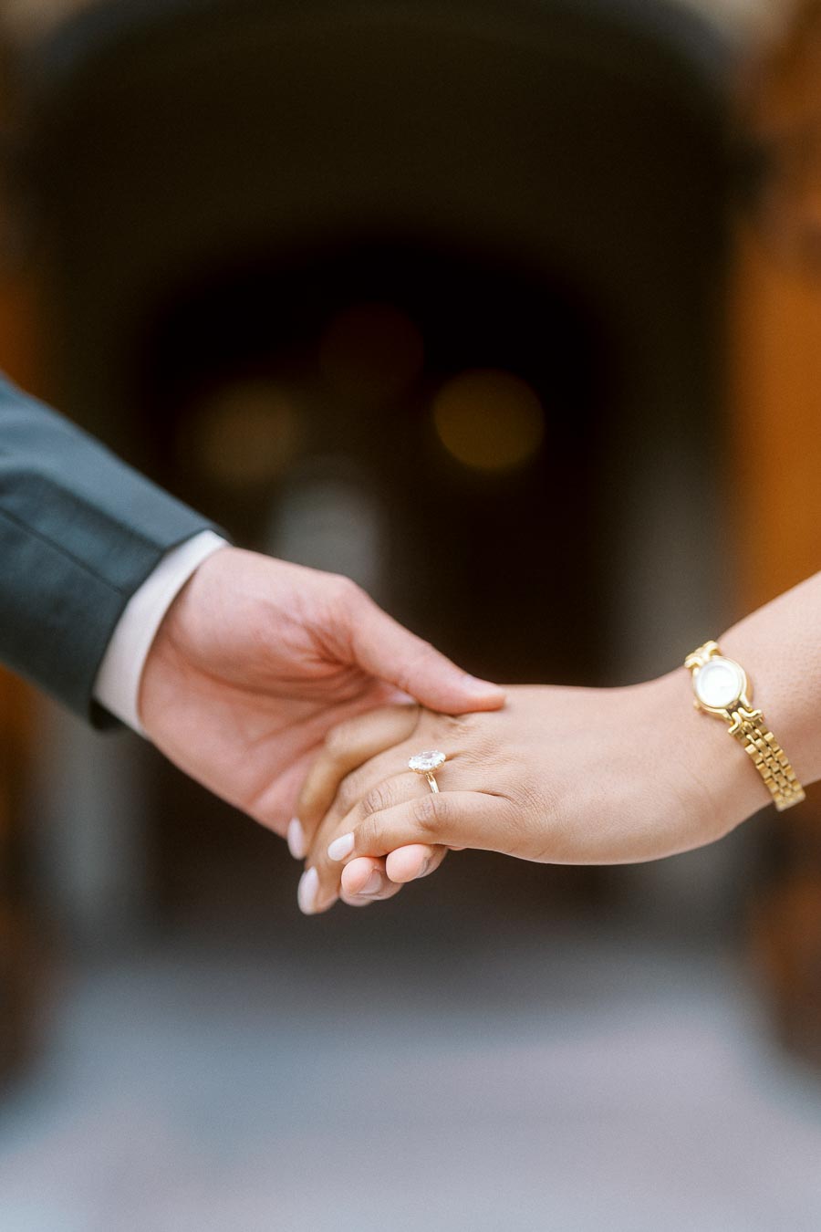 Close-up of two hands gently holding, with an engagement ring visible on one hand, photographed at the University of Toronto.