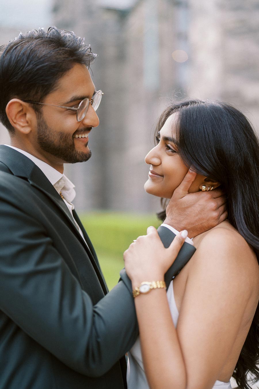 Tej and Priyana stand close together, gazing into each other's eyes, with historic stone architecture in the background at the University of Toronto.
