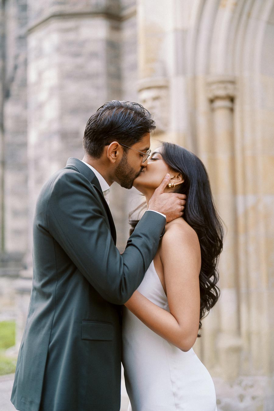 A couple shares a romantic kiss in front of stone archways at the University of Toronto St. George campus.