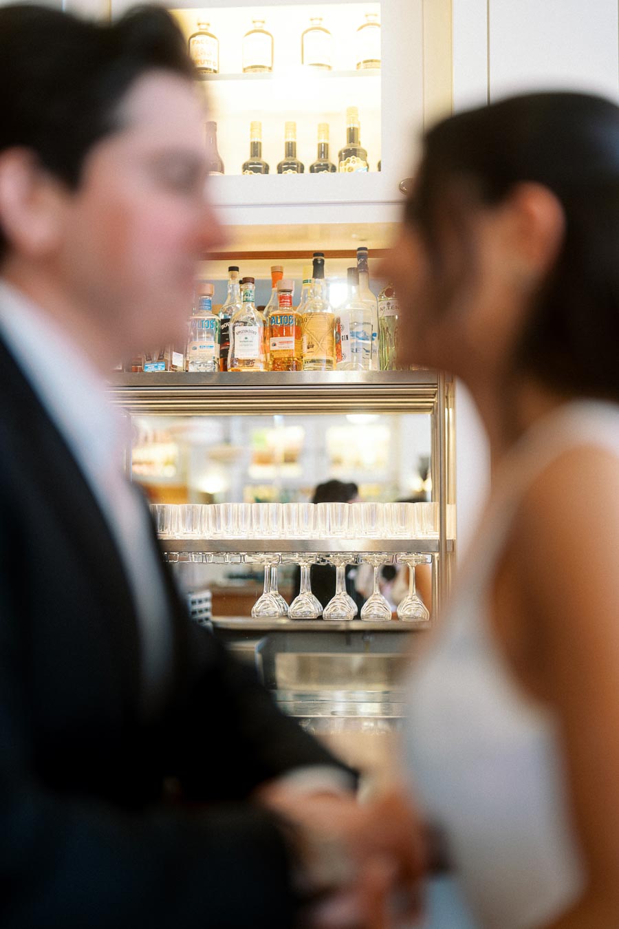 Soft-focus image of a couple facing each other and holding hands at a bar in Ontario, with bottles and glasses in the background.