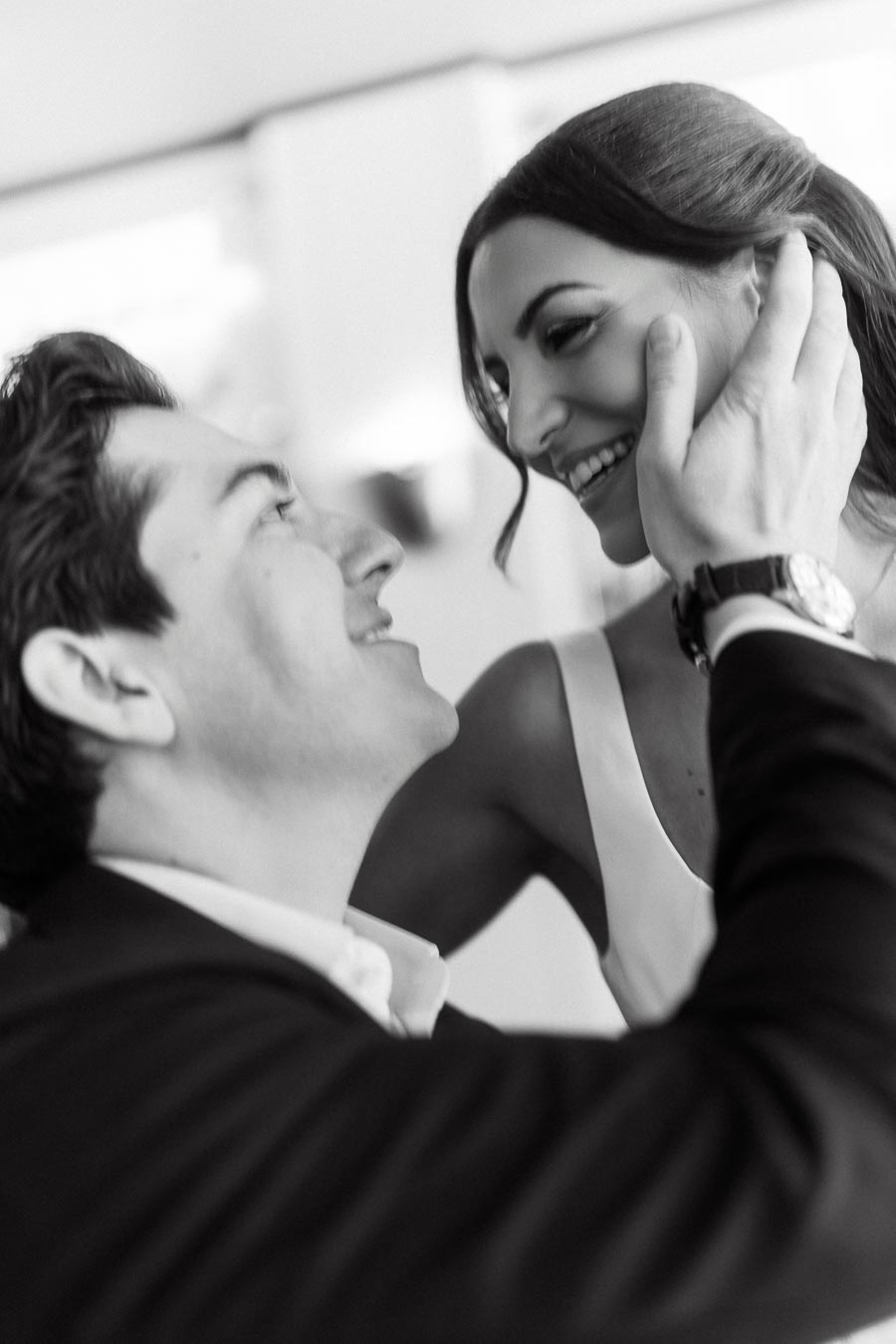 A close-up black and white photo of a smiling couple gazing at each other lovingly, the man gently touching the woman's face.
