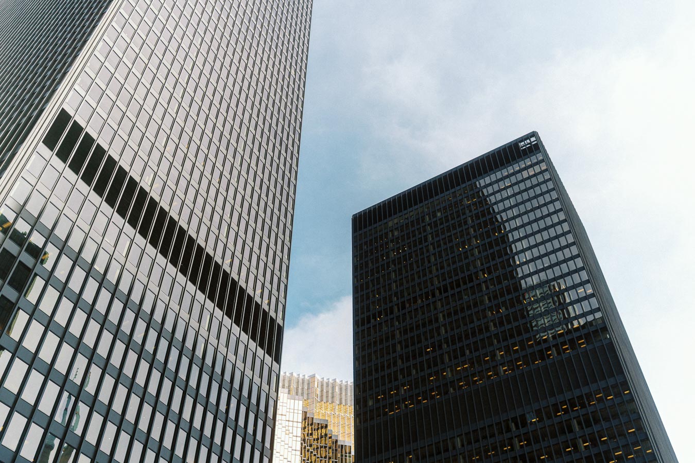 Tall modern office towers with glass windows rise into a blue sky in downtown Ontario, Canada, with reflections and geometric patterns visible.