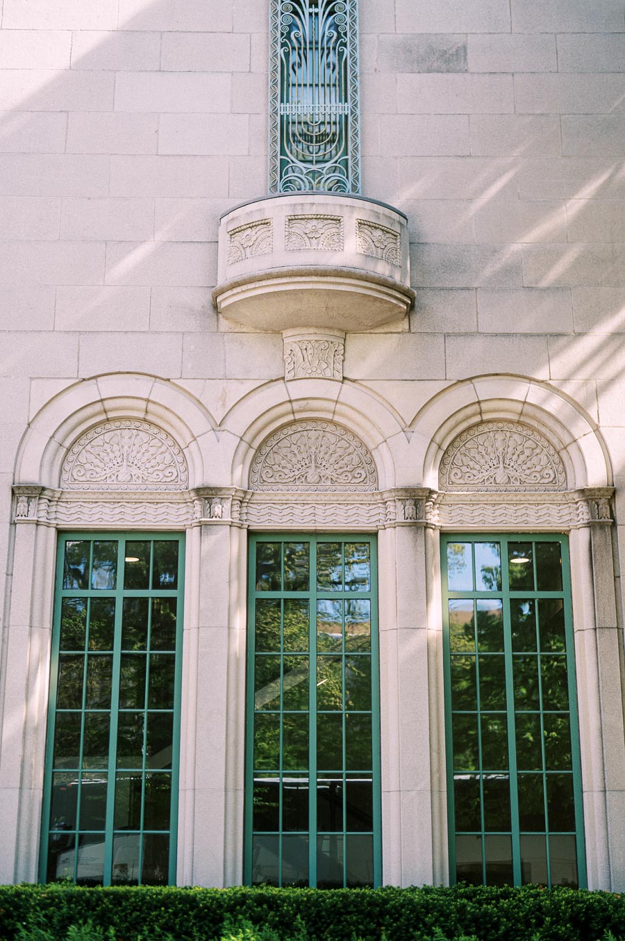 Stone building facade with three arched windows, decorative carvings, and greenery reflected in glass at Trillium Park, Toronto waterfront.