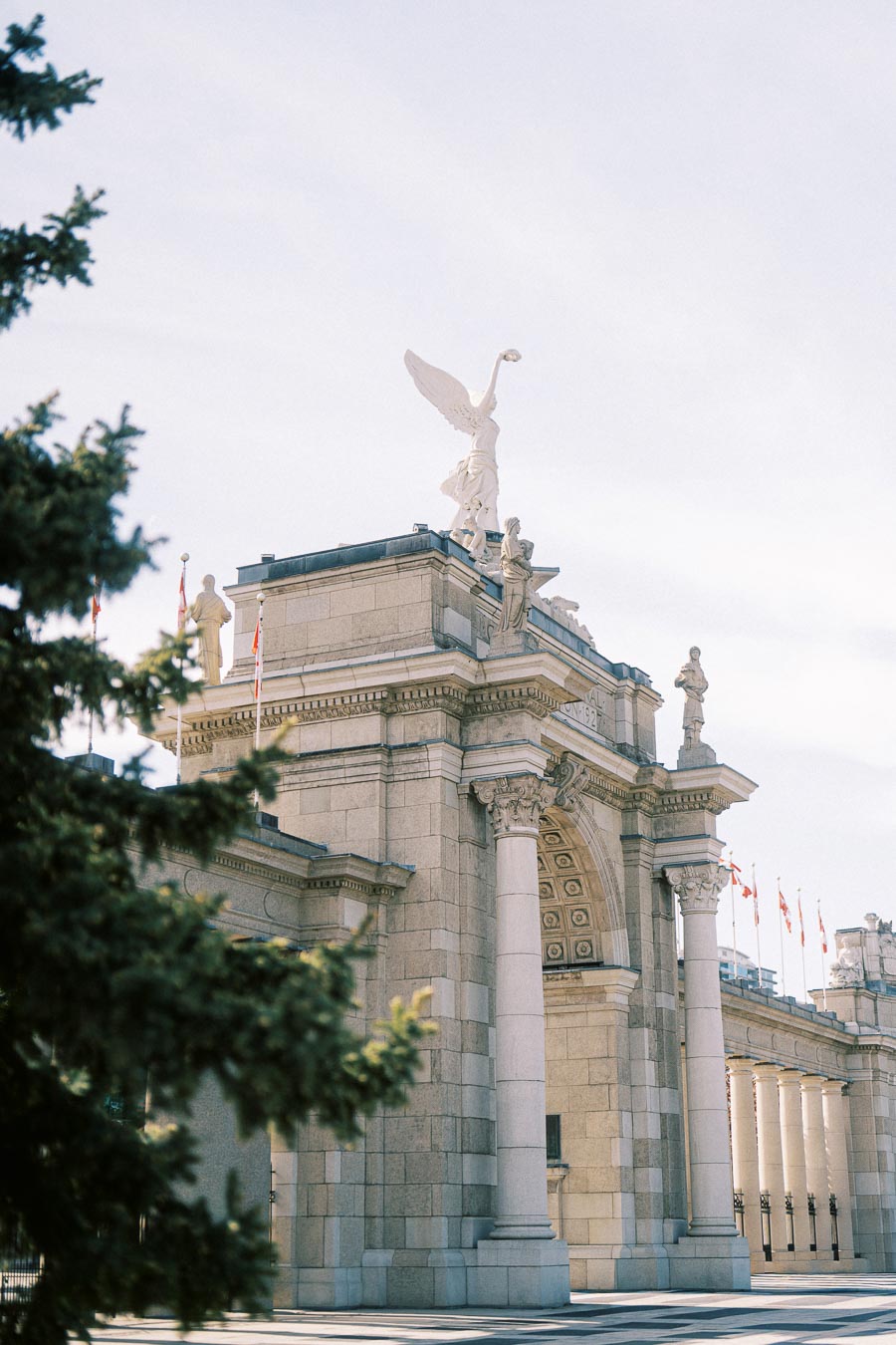 The Princes' Gates at Exhibition Place in Toronto, with detailed stone columns and statues, captured on a bright spring day with soft sunlight.