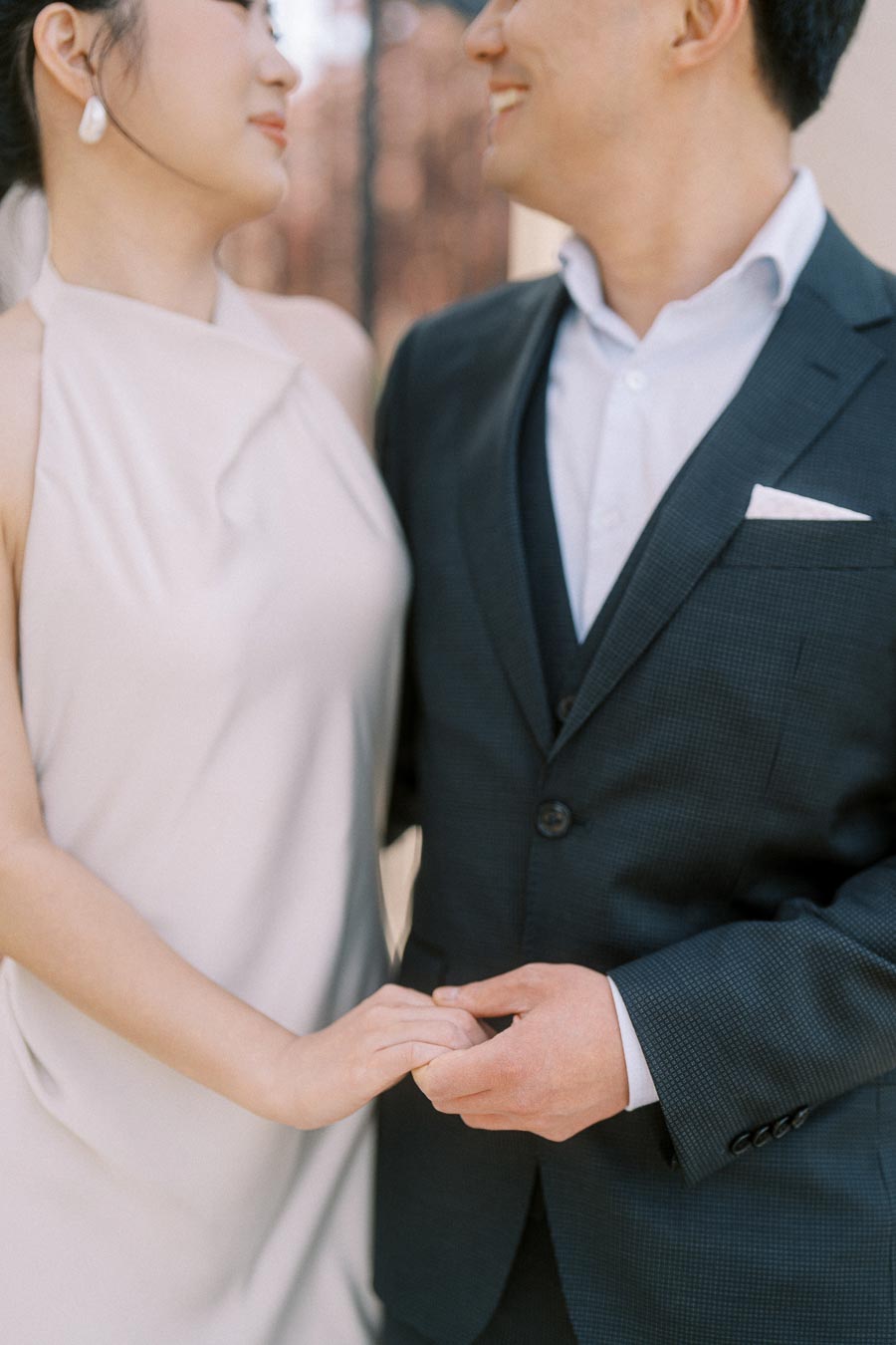 Close-up of an Asian engaged couple at Trillium Park, Toronto, smiling at each other and gently holding hands, wearing elegant formal outfits.