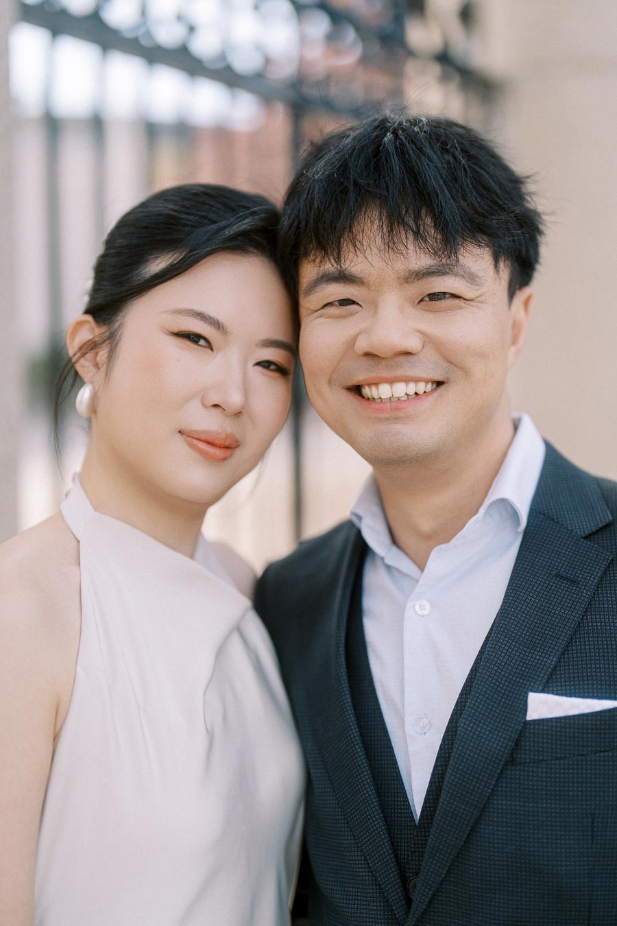Close-up of an Asian engaged couple smiling together outdoors at Trillium Park in Toronto, with soft sunlight and elegant attire visible.