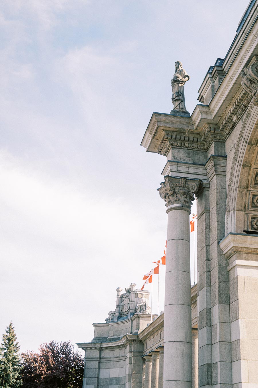 Close-up of the Princes' Gates at Exhibition Place in Toronto, showing stone columns, statues, and Canadian flags on a clear spring day.